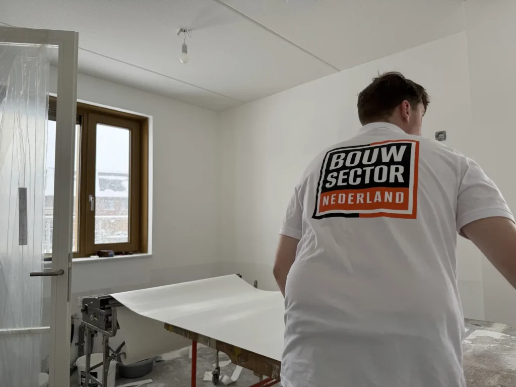 Behanger van Bouwsector Nederland in wit shirt legt een baan vlies klaar op de plaktafel in een kale nieuwbouwkamer