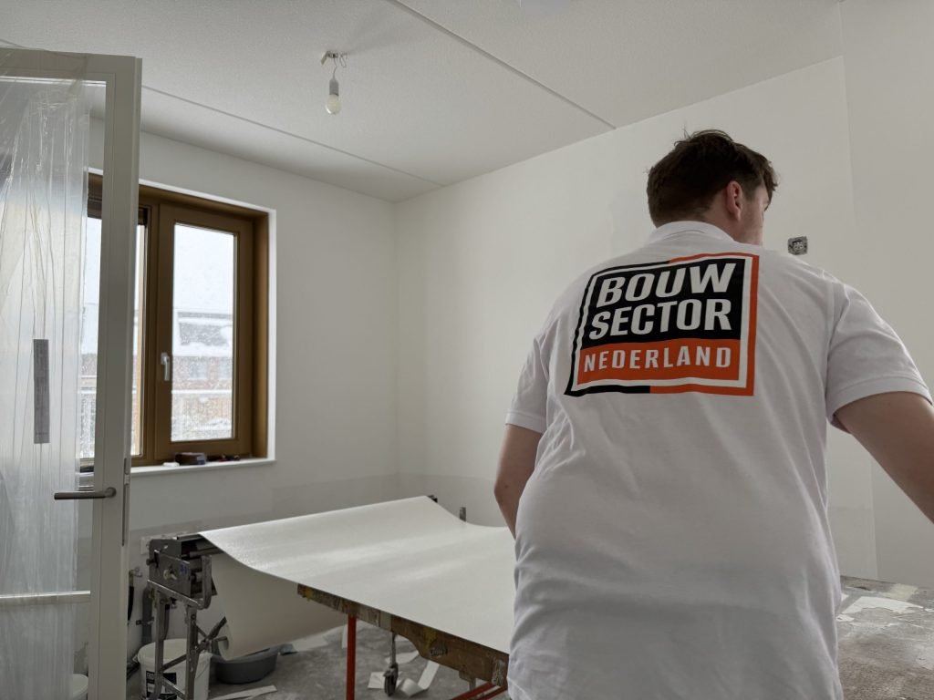 Vakman van Bouwsector Nederland met een baan behang op de plaktafel in een lege kamer