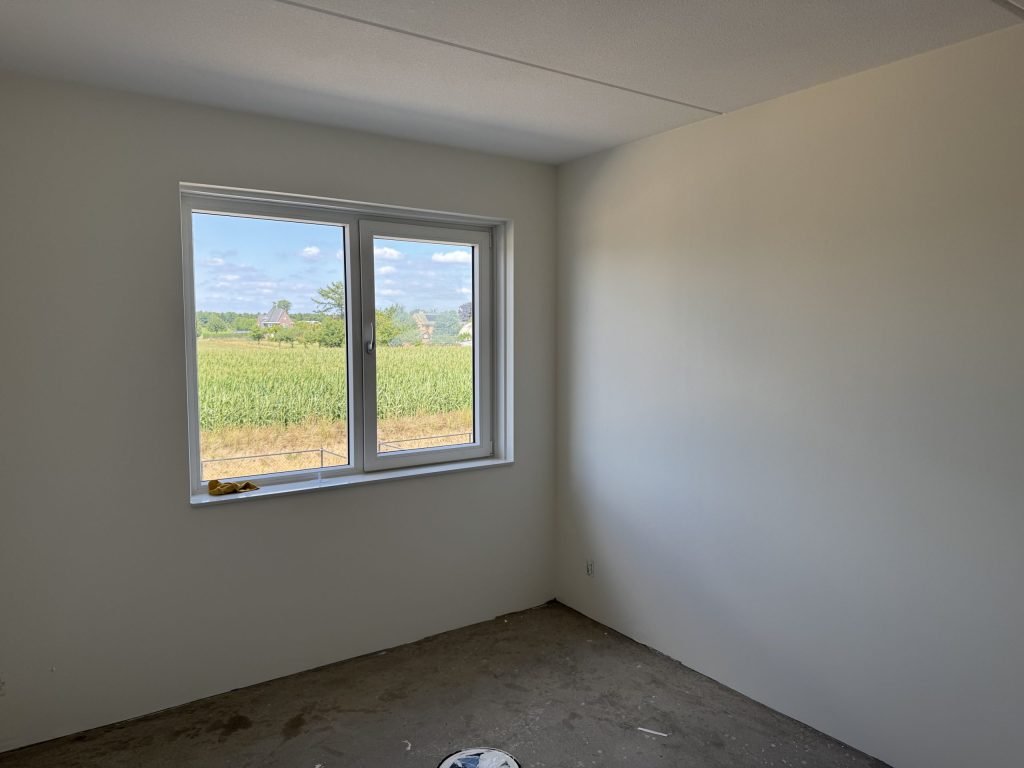 Lege slaapkamer in een nieuwbouwwoning met gladde, lichte wanden en een raam