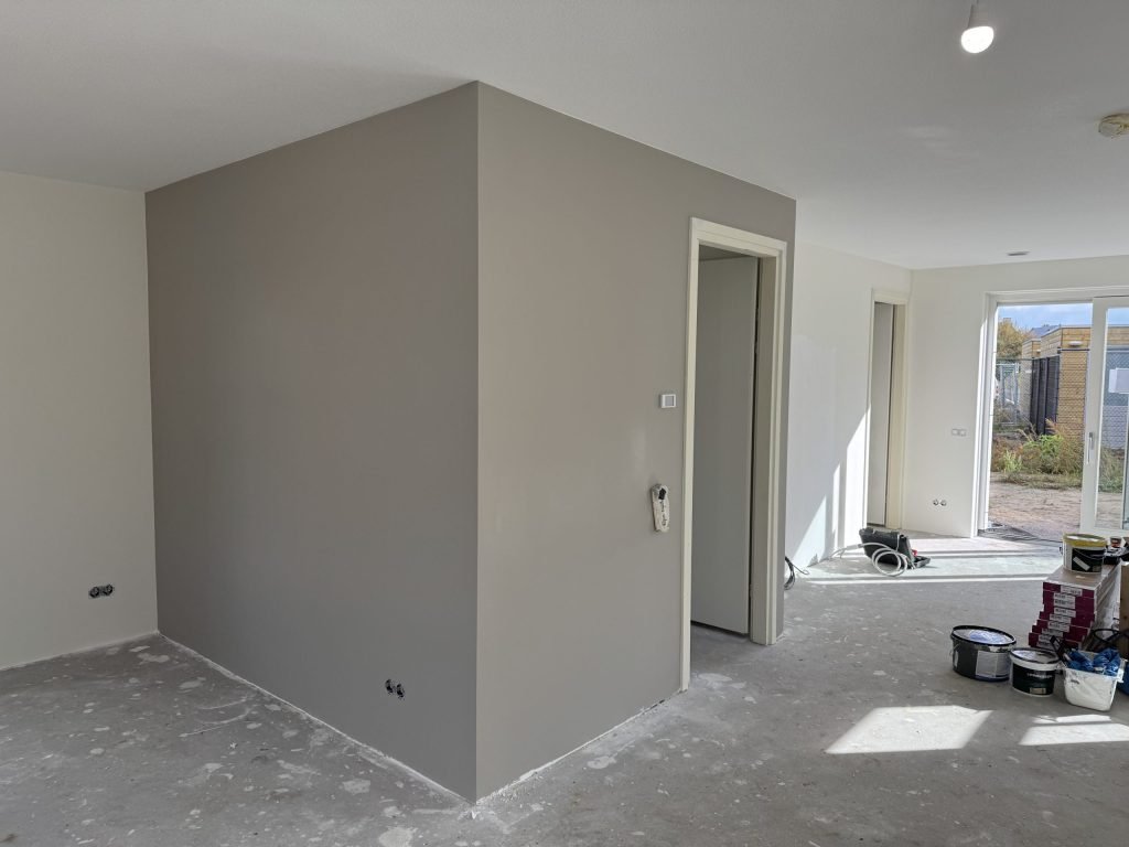 Nieuwbouwwoning met een strak afgewerkte grijze wand rond de trapkast en verfemmers op de vloer